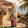 Floral-patterned water bottle on a stone ledge with plants and a building in the background