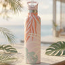 Tropical patterned water bottle on a wooden surface with blurred beach background
