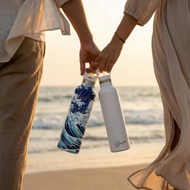 Two people holding hands with branded water bottles on a beach at sunset.