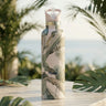 Water bottle with peacock design on a table with palm leaves in the background