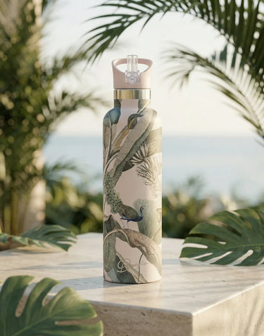 Water bottle with peacock design on a table with palm leaves in the background
