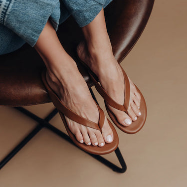 Brown sandals worn by a person sitting on a brown chair with a blurred background