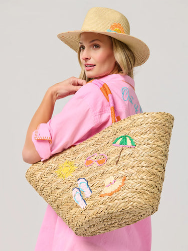 Woman holding a straw bag with beach-themed embroidery against a gray background