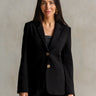 a woman wearing a black blazer with gold button accents and black pants with a white stripe on a neutral background