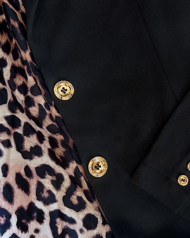 a woman wearing a black blazer with gold button accents and black pants with a white stripe on a neutral background
