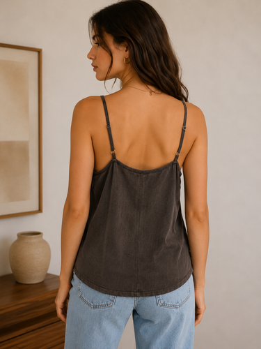 Woman wearing a dark brown tank top and light blue jeans in a room with a vase and framed picture.