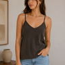 Woman wearing a dark gray tank top and blue jeans indoors.