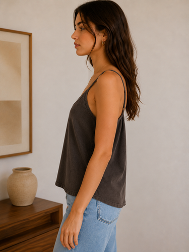 Woman wearing a dark tank top and light blue jeans standing in a room with a wooden shelf and framed abstract art.