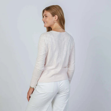 Woman wearing a light pink sweater and white pants against a plain background