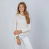 Woman wearing a light pink sweater and pants against a light gray background