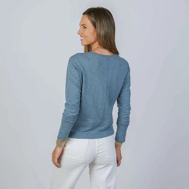 Woman wearing a blue long-sleeve top and white pants on a light gray background