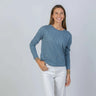 Woman wearing a blue long sleeve tee and white pants against a plain background