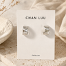 A pair of hammered cuff silver hoops on a branded ‘Chan Luu’ cardstock on an aesthetic background