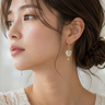 A woman wearing swirl pearl heart earrings with gold hardware on a white background.