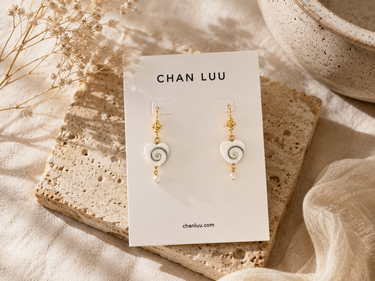 a pair of pearl heart earrings with a swirl design with gold hardware on a neutral background.