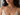 A close-up of a woman wearing a delicate beaded necklace with a gold clasp and a small dark stone pendant, paired with a cream lace camisole.