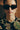 Person wearing dark sunglasses and an embroidered top with a blurred background