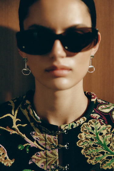 Person wearing dark sunglasses and an embroidered top with a blurred background