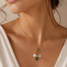 A close-up of a woman wearing a delicate gold necklace with a unique charm featuring white pearls, a blue stone, and a dark teardrop bead.