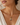 A close-up of a woman wearing a delicate gold necklace with a unique charm featuring white pearls, a blue stone, and a dark teardrop bead.