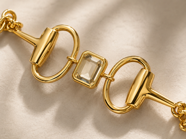 A gold horsebit chain bracelet with a clear square-cut gemstone in the center