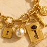 A gold-tone charm bracelet featuring a chunky link chain and multiple dangling charms, including a lock, key, shell, and coin on a neutral  background