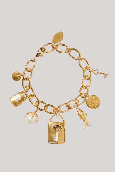 A gold-tone charm bracelet featuring a chunky link chain and multiple dangling charms, including a lock, key, shell, and coin, displayed on a neutral light gray background.