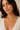 A close-up of a woman wearing a delicate gold chain necklace with a small teardrop-shaped blue pendant, styled with a white V-neck top against a soft beige background.