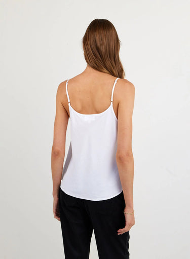 Woman wearing a white tank top and black pants on a light gray background