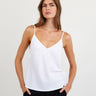 Woman wearing a white spaghetti strap top against a plain background