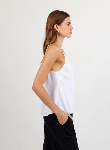 Woman wearing a white sleeveless top and black pants against a plain background