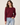 A woman wearing a burgundy knit sweater and light blue jeans, photographed from the back against a plain light beige studio background.