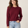 A woman wearing a burgundy knit sweater and light blue jeans, photographed from the back against a plain light beige studio background.