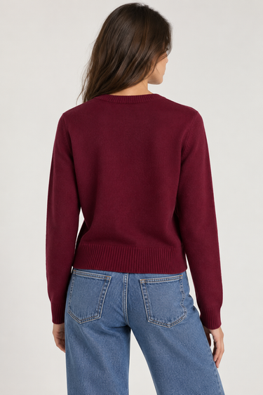 A woman wearing a burgundy knit sweater and light blue jeans, photographed from the back against a plain light beige studio background.
