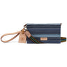 A Consuela wristlet clutch in a blue and navy striped fabric, featuring a tan leather wristlet strap and a matching leather hangtag, with a colorful woven strap detail.