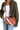 A woman wearing an olive green shirt and blue jeans carries a brown embossed leather crossbody bag with a beige strap and a colorful striped shoulder strap detail.