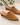 A pair of tan suede mule heels with pointed toes and low block heels, displayed on a light stone surface with green leaves in the top left. The brand name 'CORDANI ITALY' is printed on the insole.