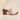 A single women's slide sandal with a chunky wooden block heel, a glittery champagne strap, and bronze-toned metal studs, set against a neutral beige background with soft leaf shadows.