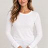 A woman wearing a Pearl white long-sleeve crewneck knit top and blue jeans, standing against a light gray studio background.
