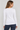 A woman shown from the back wearing a fitted white long-sleeve top and dark blue jeans against a light gray studio background.