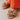 Beige sandals with floral designs worn by a person in orange pants.