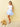 Woman in a white top and blue floral skirt standing next to a dog against a beige wall.