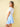 Woman wearing a white top and blue floral skirt against a beige wall