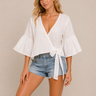 Woman wearing a white blouse with ruffled sleeves and denim shorts on a beige background