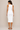 Woman wearing a white sleeveless dress against a beige background