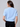 a woman facing backwards  wearing a blue knit short sleeve sweater with sparkling floral embellishments and black pants on a neutral background