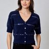 A woman wearing a navy short sleeve v-neck cardigan with blue sequin stripes and black jeans on a neutral background