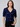 A woman wearing a navy short sleeve v-neck cardigan with blue sequin stripes and black jeans on a neutral background