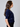A woman wearing a navy short sleeve v-neck cardigan with blue sequin stripes and black jeans on a neutral background
