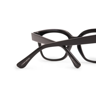 Black eyeglasses with 'Compliments' branding on a white background